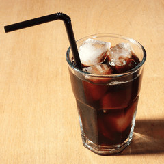 Foto segelas es kopi hitam dengan es batu dan sedotan hitam di meja kayu terang