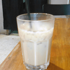Foto segelas es latte susu dengan es batu dan sedotan hitam di meja kayu