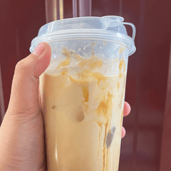 Foto es kopi susu gula aren dalam gelas plastik bening dengan tutup, dipegang tangan