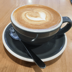 Foto kopi susu panas dengan latte art hati di cangkir hitam dan tatakan